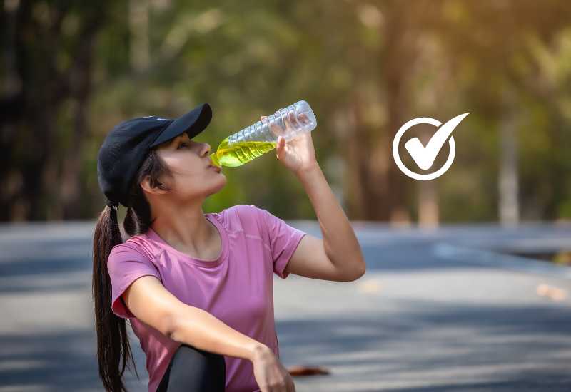 wanita sedang duduk & minum dari air botol sehabis olahraga